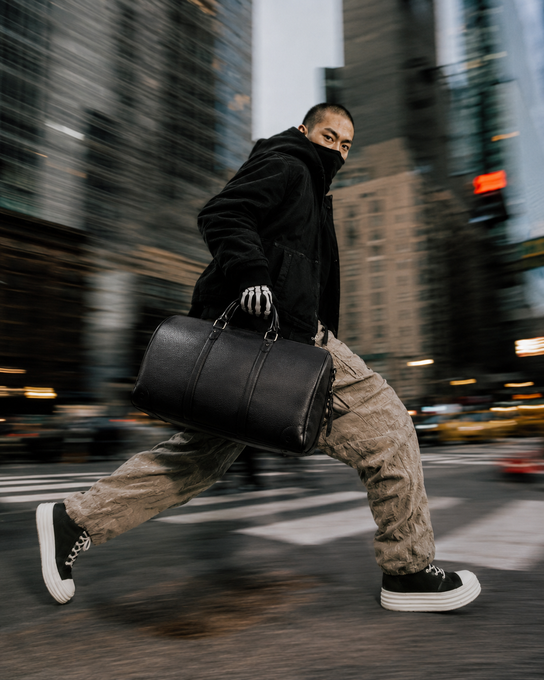 A man runs across a city street carrying a black AC47 Carry duffel bag.