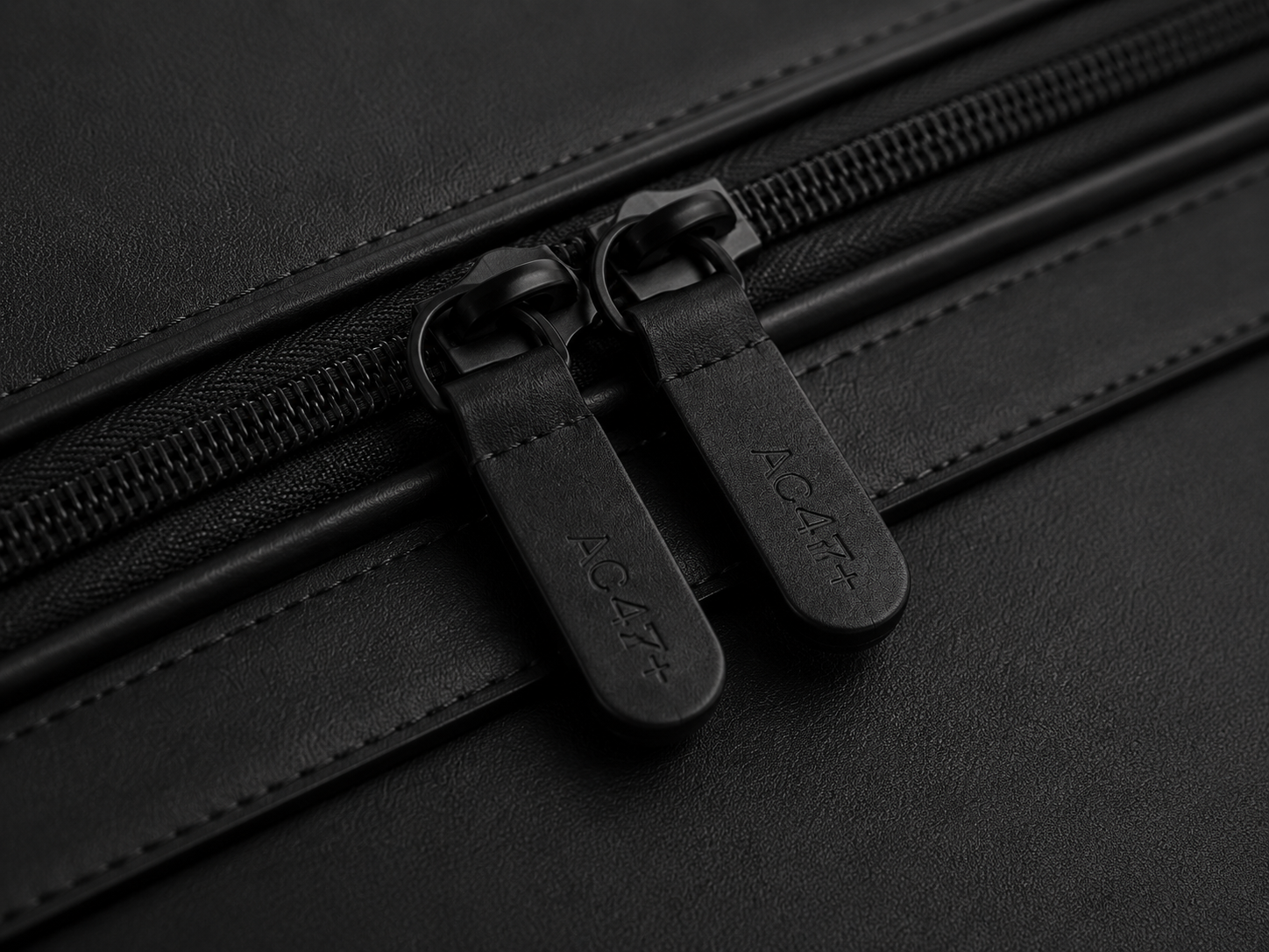 Close view of paired leather-tabbed zipper pulls on a black panel.